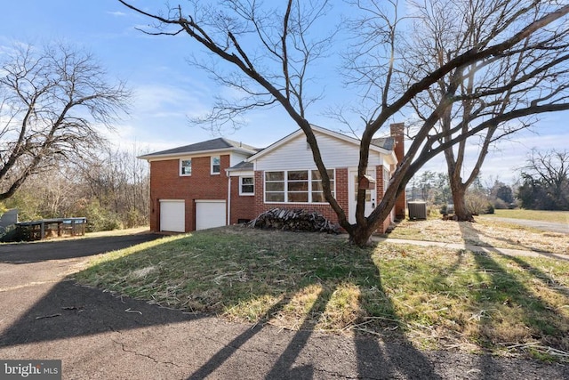 view of front of house featuring driveway, a garage, brick siding, central AC unit, and a chimney