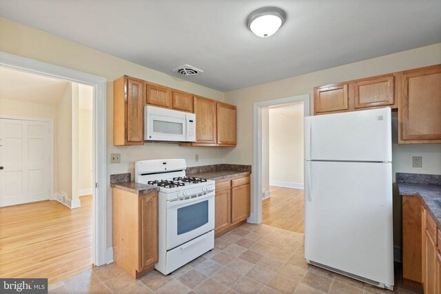 kitchen featuring dark countertops, visible vents, white appliances, and baseboards