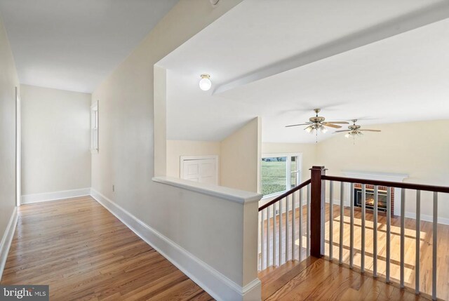 corridor featuring baseboards, an upstairs landing, and wood finished floors