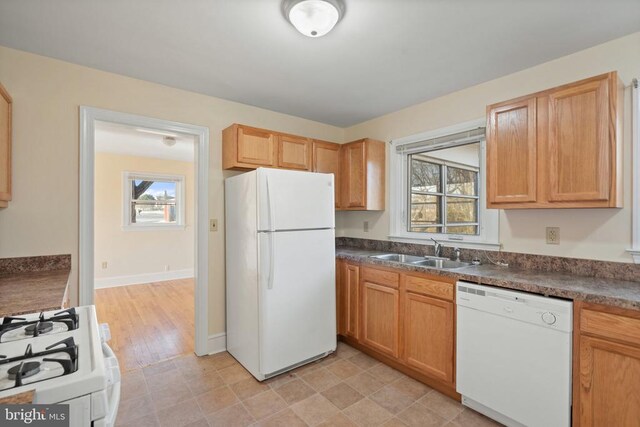 kitchen featuring white appliances, dark countertops, baseboards, and a sink