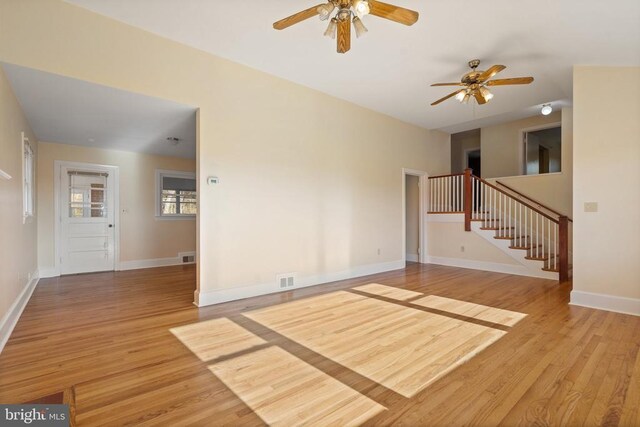 unfurnished living room featuring a ceiling fan, visible vents, baseboards, stairs, and light wood-style floors