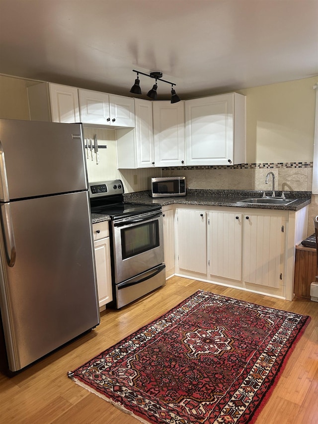 kitchen featuring dark countertops, a sink, light wood finished floors, stainless steel appliances, and backsplash