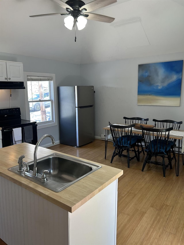 kitchen featuring electric range, a sink, butcher block countertops, freestanding refrigerator, and under cabinet range hood
