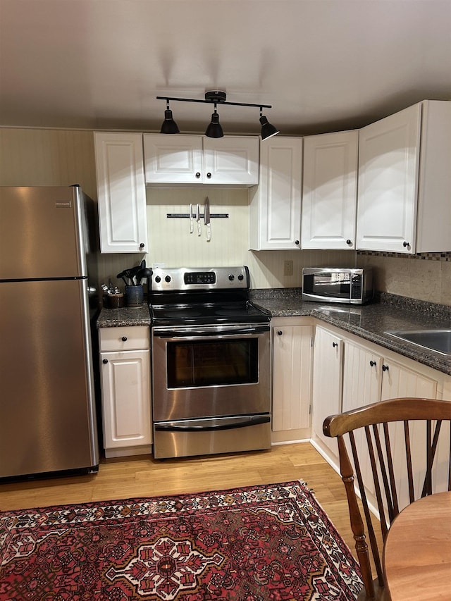 kitchen with dark countertops, light wood-style floors, white cabinets, a sink, and stainless steel appliances