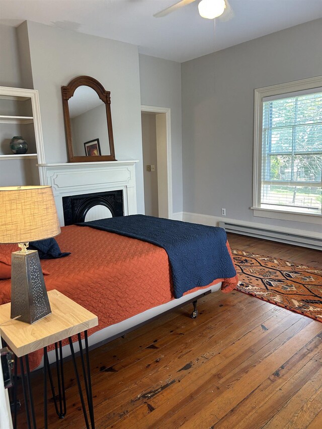 bedroom with ceiling fan, a baseboard heating unit, hardwood / wood-style flooring, and a fireplace