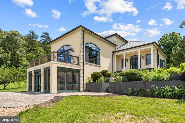 rear view of property with a balcony, a sunroom, and a lawn