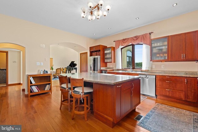 kitchen featuring appliances with stainless steel finishes, a notable chandelier, light stone countertops, light hardwood / wood-style floors, and a kitchen island