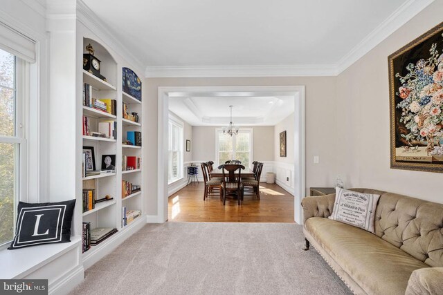 carpeted living room with built in features, ornamental molding, a raised ceiling, and a chandelier