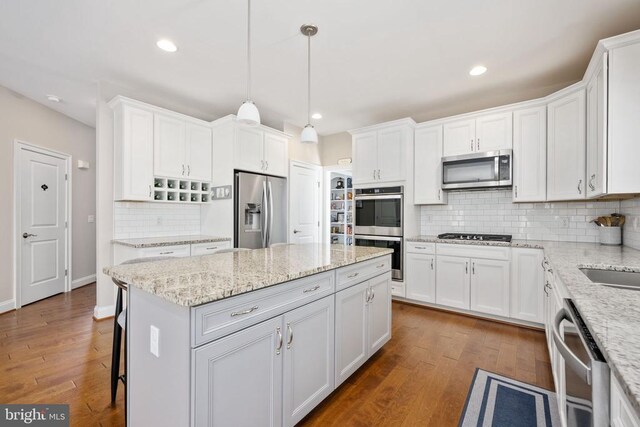 kitchen with appliances with stainless steel finishes, light stone counters, white cabinets, a kitchen island, and decorative light fixtures