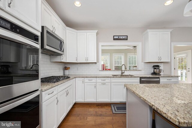 kitchen with dark hardwood / wood-style floors, white cabinetry, sink, stainless steel appliances, and light stone countertops