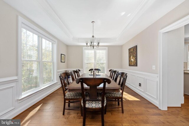 dining area featuring crown molding, an inviting chandelier, light wood-type flooring, and a tray ceiling