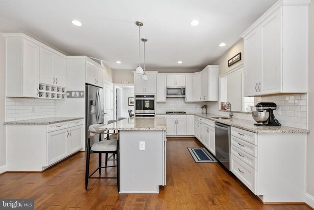 kitchen with a kitchen island, white cabinetry, appliances with stainless steel finishes, and hanging light fixtures