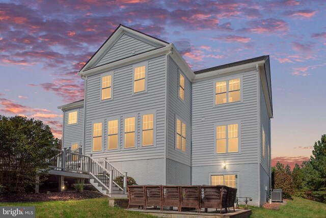 back house at dusk featuring central AC unit, a lawn, outdoor lounge area, and a deck