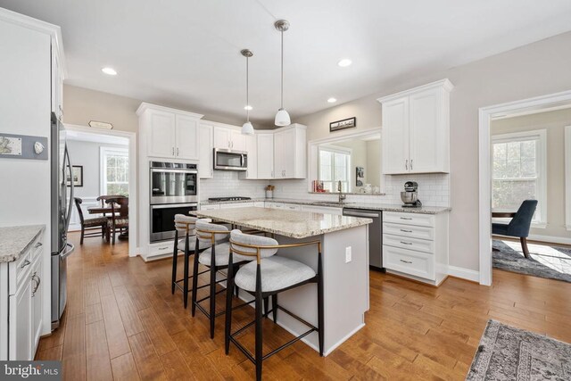 kitchen featuring white cabinetry, appliances with stainless steel finishes, a center island, and light stone counters