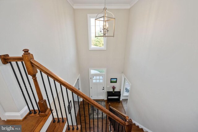 staircase with ornamental molding, wood-type flooring, a chandelier, and a high ceiling