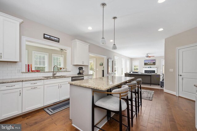 kitchen with sink, white cabinetry, light stone counters, hanging light fixtures, and a kitchen island