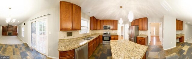 kitchen with hanging light fixtures, stainless steel appliances, sink, and light stone countertops