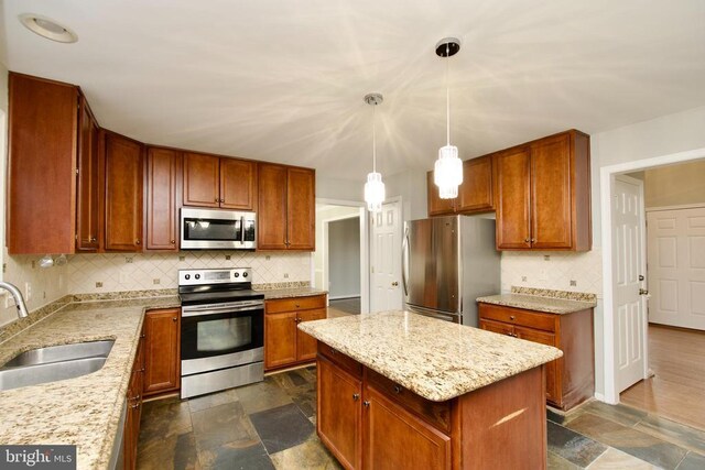 kitchen with sink, appliances with stainless steel finishes, light stone counters, a kitchen island, and decorative light fixtures