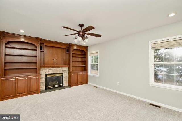 unfurnished living room featuring a stone fireplace, carpet floors, and ceiling fan