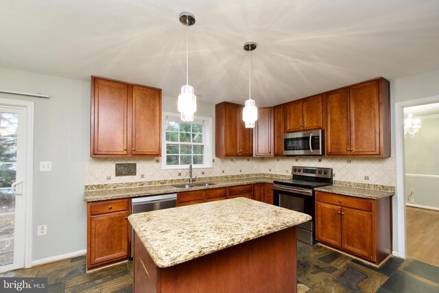 kitchen featuring sink, stainless steel appliances, light stone countertops, a kitchen island, and decorative light fixtures