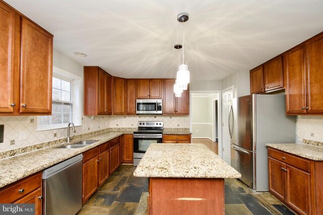 kitchen featuring sink, light stone counters, a kitchen island, pendant lighting, and stainless steel appliances