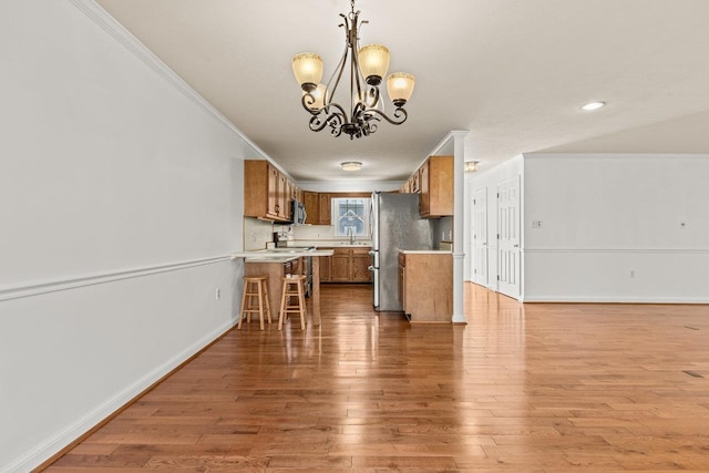 kitchen featuring brown cabinets, wood finished floors, appliances with stainless steel finishes, crown molding, and light countertops