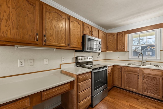 kitchen with brown cabinets, a sink, light wood-style floors, appliances with stainless steel finishes, and light countertops