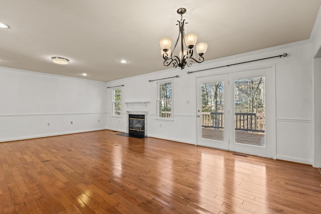 unfurnished living room featuring visible vents, a premium fireplace, ornamental molding, hardwood / wood-style floors, and an inviting chandelier