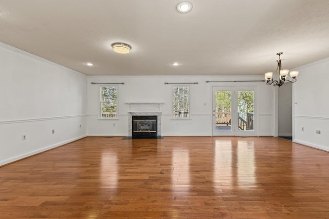 unfurnished living room with wood finished floors, baseboards, a high end fireplace, ornamental molding, and a chandelier