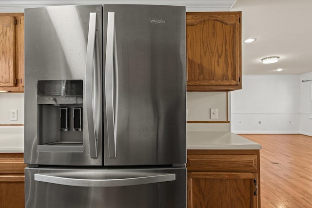 kitchen featuring stainless steel fridge, brown cabinets, wood finished floors, and light countertops