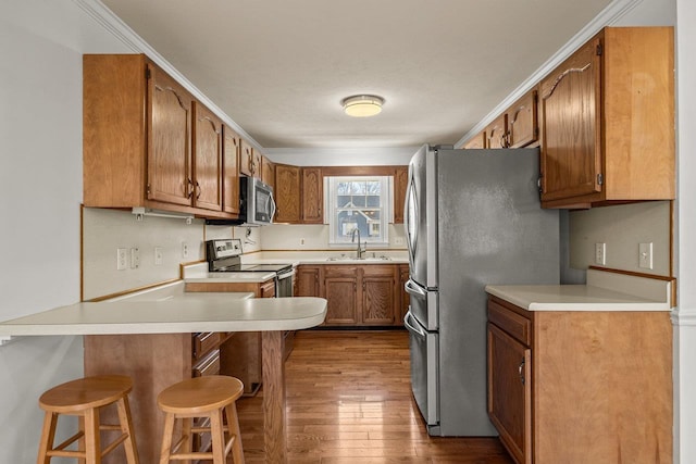 kitchen with a peninsula, a sink, dark wood-type flooring, appliances with stainless steel finishes, and a kitchen breakfast bar