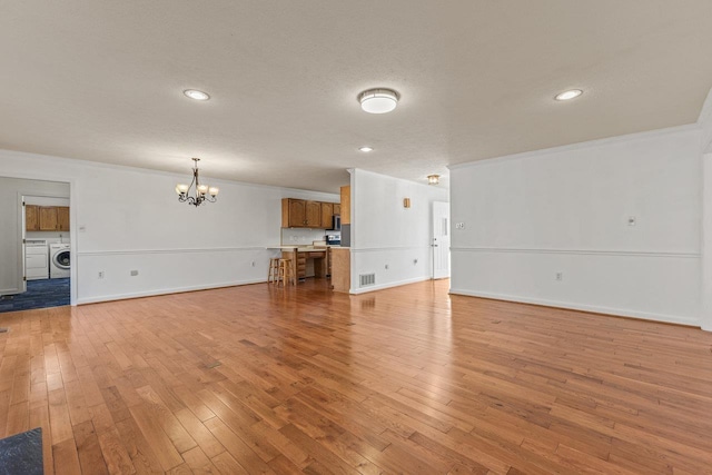 unfurnished living room featuring visible vents, light wood-style flooring, ornamental molding, washing machine and dryer, and a chandelier