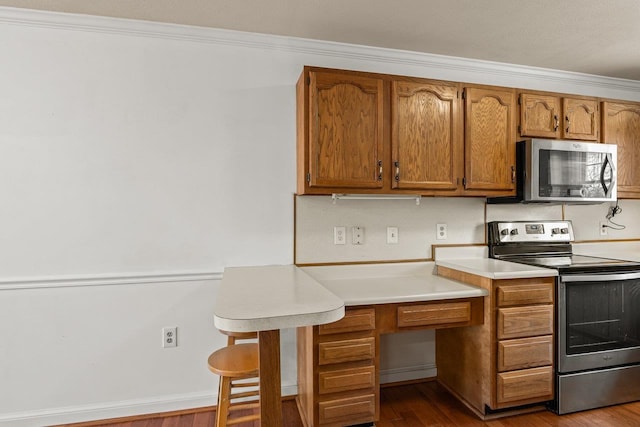 kitchen with brown cabinets, stainless steel appliances, crown molding, light countertops, and dark wood-style flooring