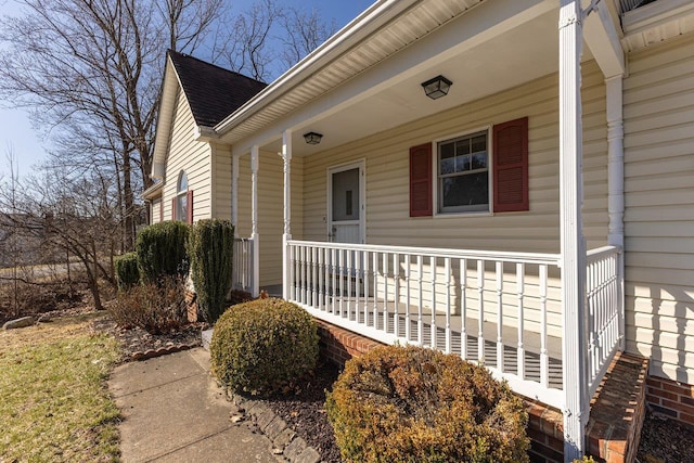 doorway to property featuring covered porch and a shingled roof