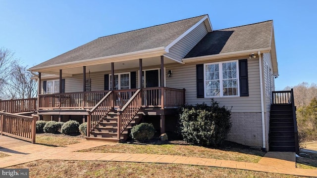 view of front facade featuring covered porch, a shingled roof, stairs, and brick siding