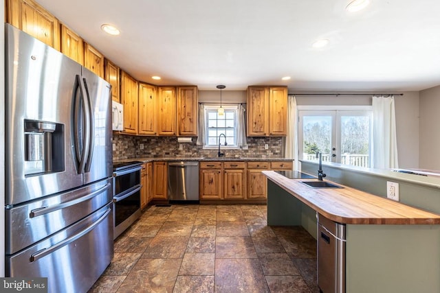 kitchen featuring decorative backsplash, decorative light fixtures, stainless steel appliances, wooden counters, and a sink