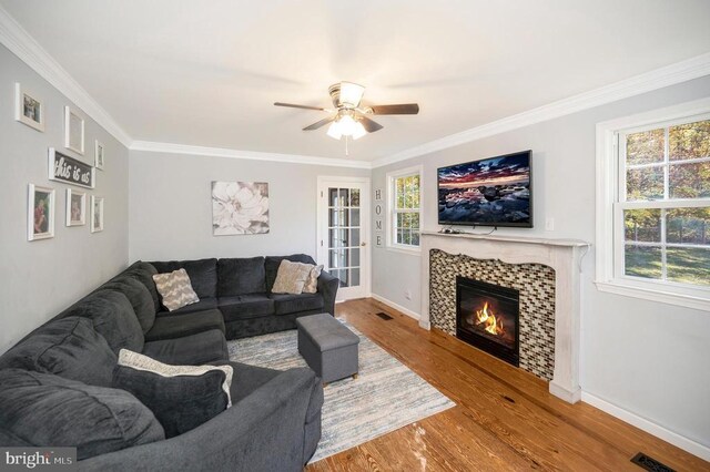 living room featuring wood-type flooring, ornamental molding, a tile fireplace, and ceiling fan