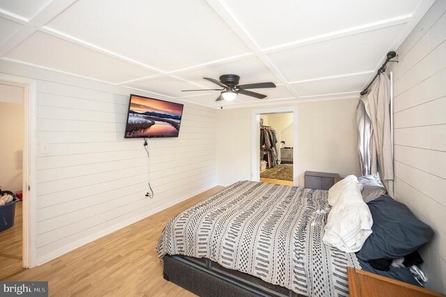 bedroom with wooden walls, coffered ceiling, hardwood / wood-style floors, and a spacious closet