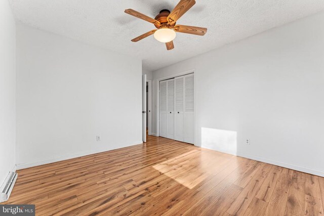 empty room featuring ceiling fan, a baseboard radiator, a textured ceiling, and light wood-type flooring