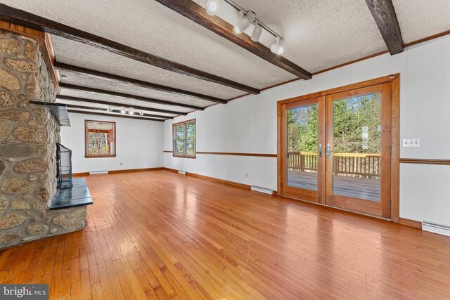 unfurnished living room featuring beamed ceiling, a baseboard heating unit, a textured ceiling, light wood-type flooring, and french doors