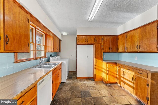 kitchen featuring washer and dryer, dishwasher, sink, backsplash, and a textured ceiling