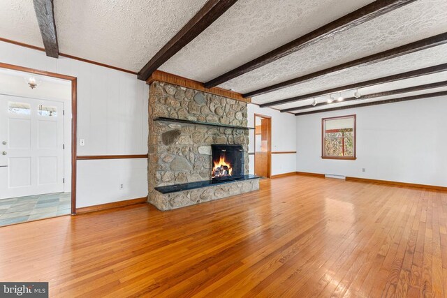 unfurnished living room with a stone fireplace, wood-type flooring, beamed ceiling, and a textured ceiling