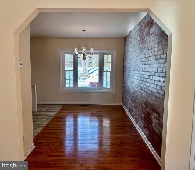 unfurnished dining area with dark wood-type flooring, brick wall, and a notable chandelier