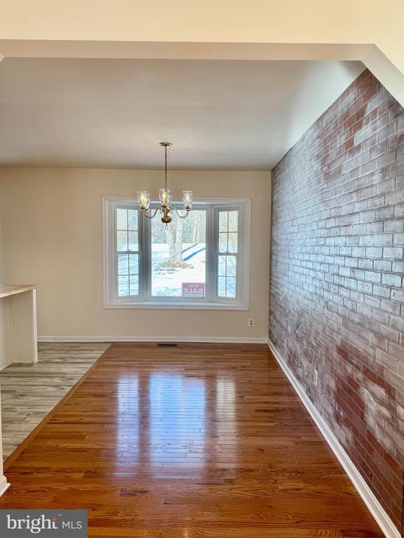 unfurnished dining area featuring wood-type flooring, brick wall, and an inviting chandelier