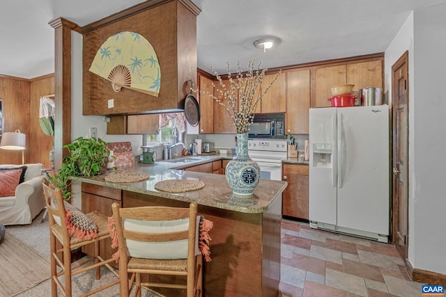kitchen with brown cabinets, a sink, white appliances, stone finish floor, and a peninsula