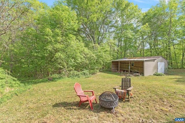 view of yard with a storage shed, a view of trees, an outbuilding, and an outdoor fire pit