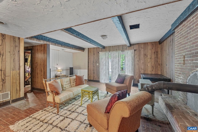 living area with wooden walls, beam ceiling, brick floor, a textured ceiling, and visible vents