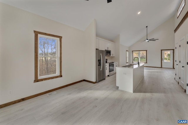 kitchen featuring high vaulted ceiling, light wood-type flooring, appliances with stainless steel finishes, an island with sink, and white cabinets