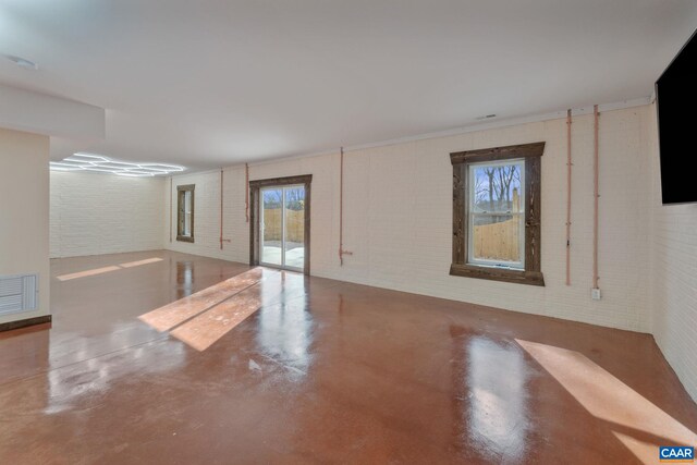 unfurnished room featuring brick wall, a wealth of natural light, and concrete floors