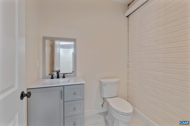 bathroom featuring vanity, toilet, and brick wall